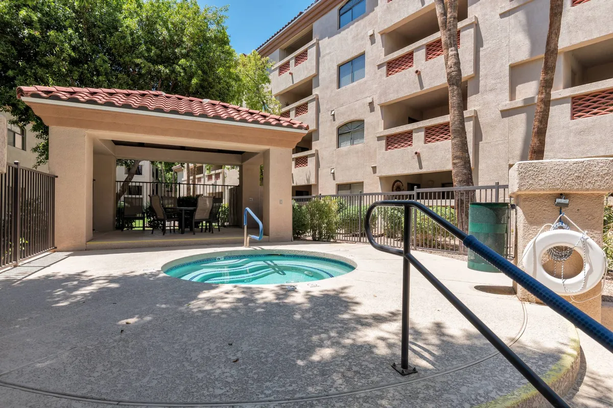 A spacious outdoor hot tub area featuring inviting seating, well-maintained landscaping, and the building facade in the background. The area is well-lit, designed for socializing or quiet relaxation under the open sky.