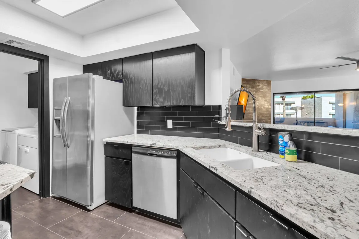 This image provides a slightly different angle of the kitchen, showcasing the large granite countertop, stainless steel appliances, and ample black cabinetry. The addition of a large sink and spacious layout emphasizes the kitchen’s suitability for both casual meal prep and hosting gatherings. The scene hints at morning coffee or preparing a family dinner, reinforcing the kitchen's dual purpose.