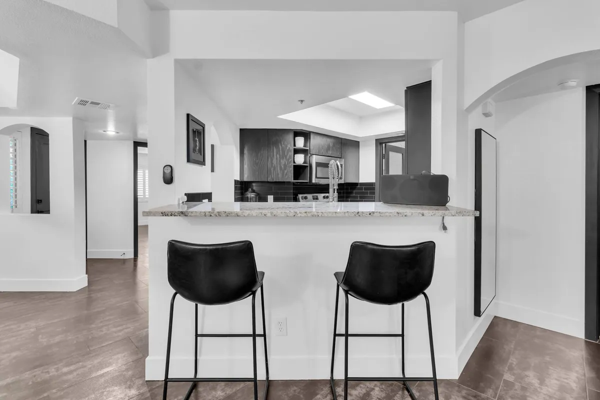 This image highlights the transition between the kitchen and dining space, with bar stools set at the granite countertop and kitchen cabinetry visible in the background. The arrangement invites casual dining and socializing, making it easy for the chef to remain part of the conversation while preparing meals.