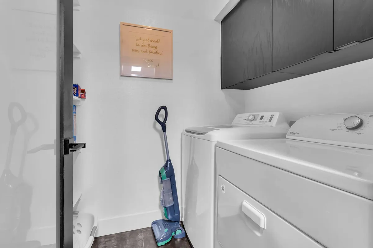 A tidy laundry room with a washing machine, dryer, cleaning supplies, and framed art. The practical setup highlights the convenience and home-like amenities available for families traveling with kids.