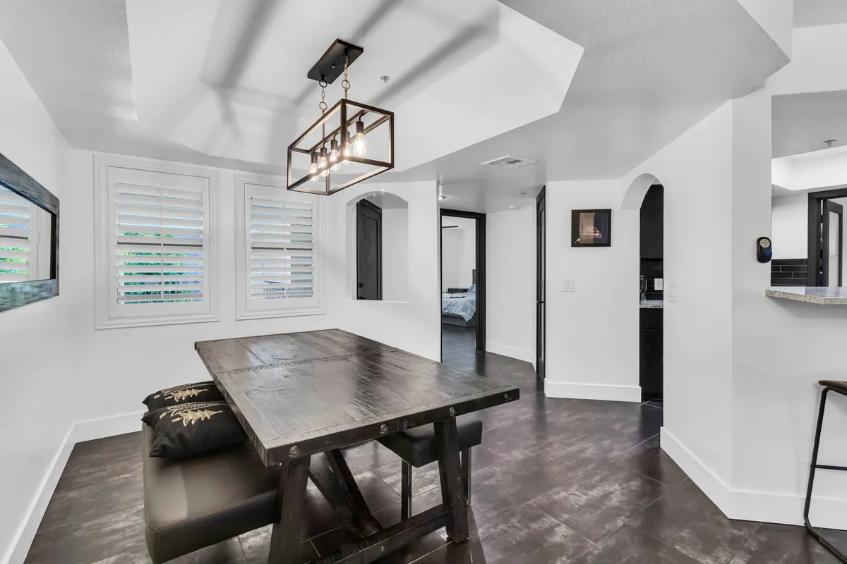 A cozy dining area with a table seating four to six, a modern chandelier, window shutters, and black cabinetry. The setting is perfect for family meals or intimate social gatherings, complementing the adjoining living and kitchen areas.