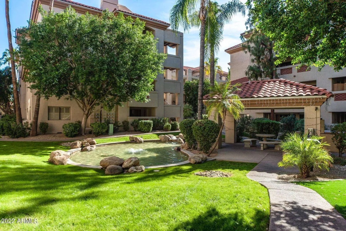 A tranquil scene featuring a lush, landscaped pond surrounded by greenery and a pavilion, with rock formations adding to the natural ambiance. The area is well-suited for relaxing, socializing, or enjoying a quiet moment outdoors, evoking a serene community atmosphere.