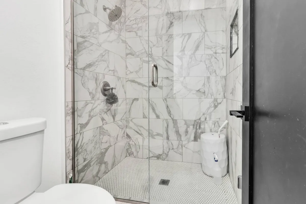 A modern bathroom featuring marble tile shower walls, a glass-enclosed walk-in shower, and sleek fixtures. The spa-like design and serene lighting invite relaxation and rejuvenation, ideal for starting or ending the day.