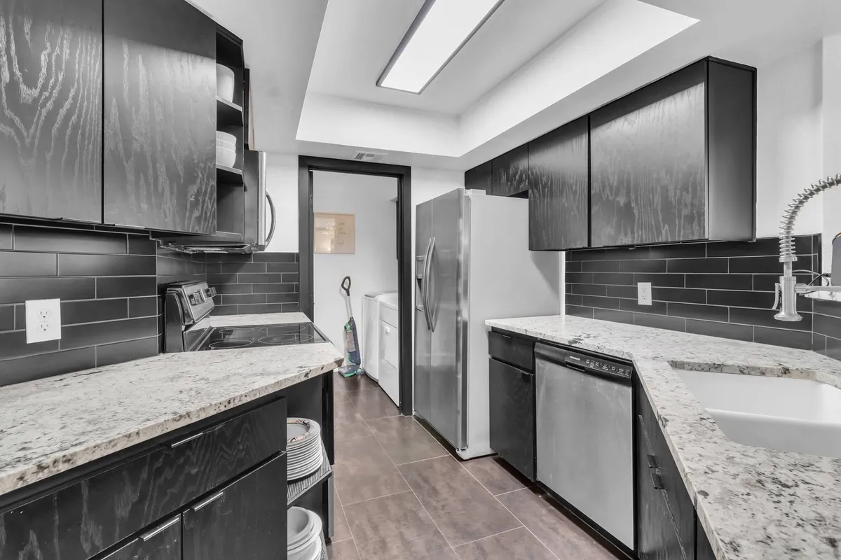 This image captures a contemporary kitchen featuring granite countertops, sleek stainless steel appliances, and striking black cabinetry. The workspace is uncluttered, with appliances and cookware easily accessible, projecting both efficiency and style. The atmosphere is warm and inviting, suggesting a space where cooking and entertaining naturally come together.