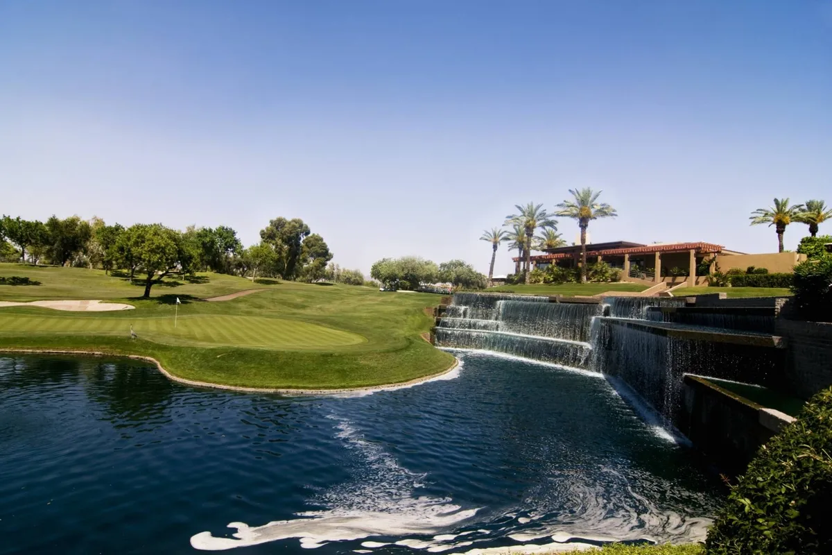 An inviting exterior view showcasing a sparkling swimming pool, palm trees, a waterfall, a golf course, and picnic-ready green spaces. The setting captures the essence of a resort-style retreat with opportunities for relaxation and outdoor activity.
